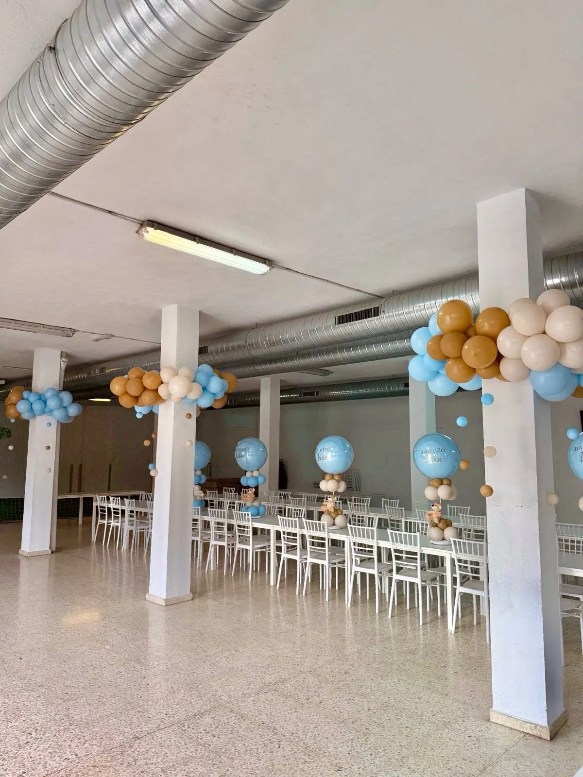 Salón de bautizo con guirnaldas de globos azules, blancos y dorados en Málaga